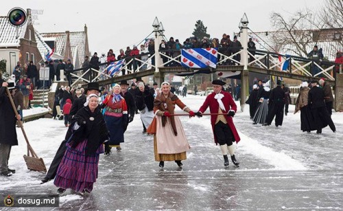 Люди в традиционной голландской одежде катаются на коньках по замёрзшему каналу в городке Hindeloopen, Нидерланды.